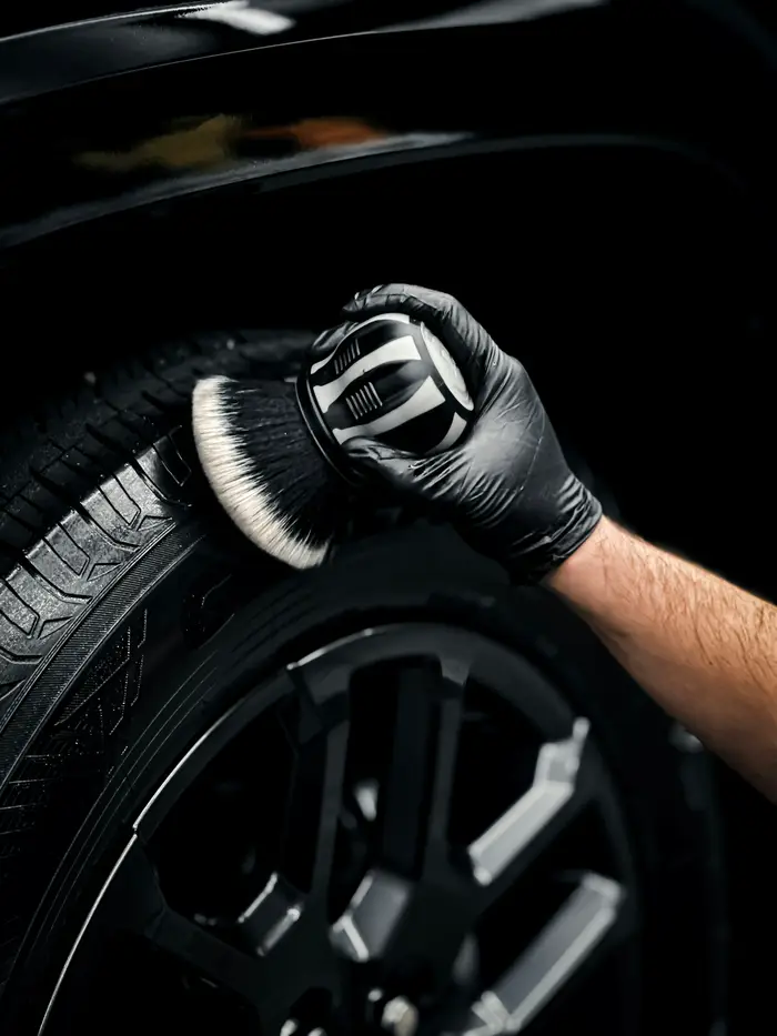 A gloved hand scrubbing a tire with a brush
