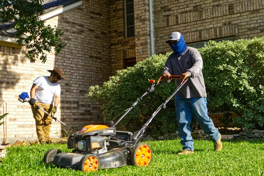 Two landscapers mowing and trimming a front lawn